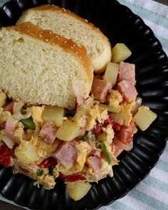 a black plate topped with eggs, ham and vegetables next to a slice of bread