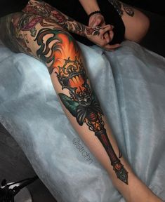 a person sitting on a bed with a tattoo on their arm and leg, holding a knife