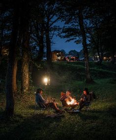 three people sitting around a campfire in the woods at night with their lights on