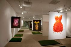 an art gallery with paintings and fake grass on the floor in front of white walls