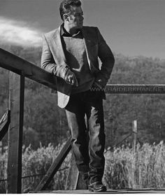 black and white photograph of a man standing on a wooden railing looking off into the distance