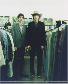 two men standing next to each other in front of clothes