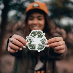 a woman holding up a green and white sticker in front of her face while wearing a hat