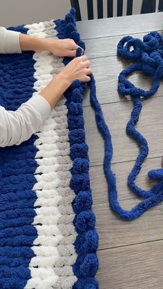 a woman is crocheting a blue and white afghan on a table with scissors