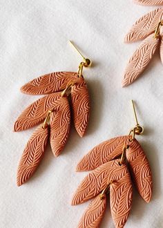 two pairs of earrings with leaves on them sitting next to each other, one in gold and the other in pink