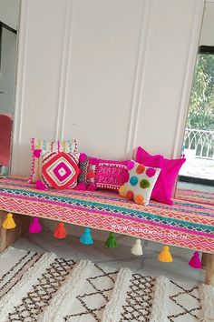 a pink bench with colorful pillows and pom - poms on it