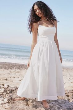 a woman standing on the beach wearing a white dress