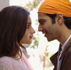 a man and woman standing next to each other with an orange bandana on their head