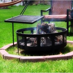 a fire pit sitting in the middle of a lush green field next to two chairs