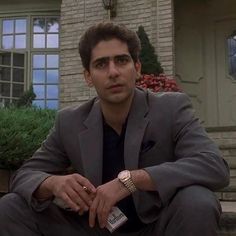 a man sitting on the steps in front of a house wearing a suit and watch