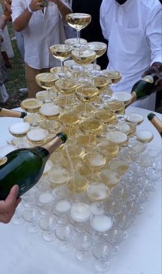 a table topped with lots of wine glasses filled with champagne and people standing around looking at them