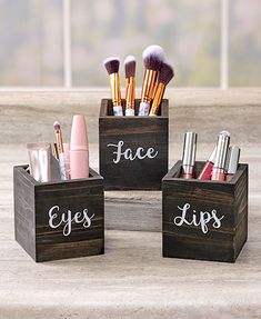 three wooden boxes with makeup brushes and eyeliners in them on a table next to a window