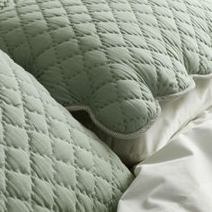 an unmade bed with green comforter and pillows