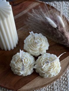 three white roses on a wooden plate next to a feather and candle holder with feathers