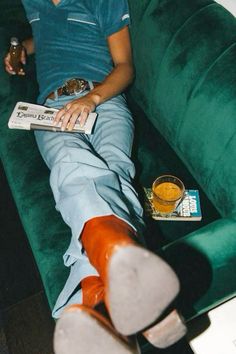 a man sitting on a green couch with his feet up and holding a book in front of him