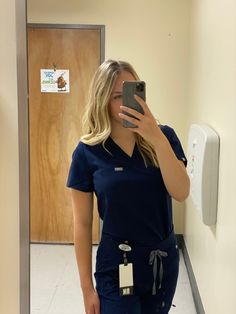 a woman in scrubs taking a selfie in the mirror with her cell phone