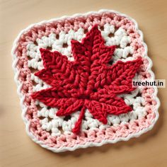 a crocheted red and white maple leaf on top of a wooden table