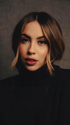 a woman with shoulder length hair wearing a black turtle neck sweater and dark lipstick looks at the camera