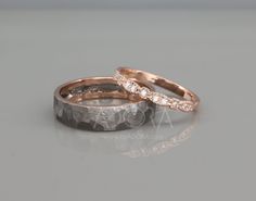 two gold wedding bands with diamonds on each band, set against a gray background and reflected in the glass