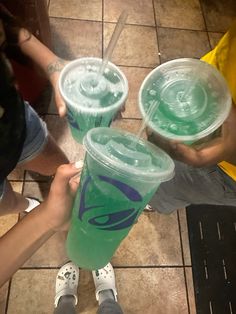 three people holding up green drinks in plastic cups with straws on the top and bottom