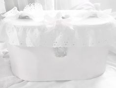 a white box sitting on top of a bed covered in sheets and pillows with bows