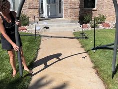 a woman standing on top of a sidewalk next to a metal pole in front of a house