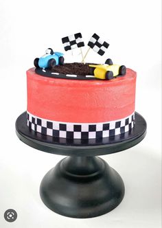 a cake decorated with race cars on top of a black stand and white checkerboard