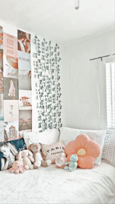 a bed with pillows and stuffed animals on it in front of a wall full of pictures