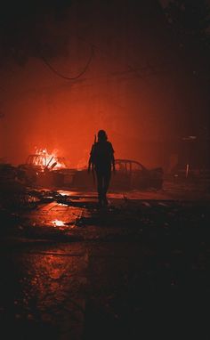 a person walking down a street at night in front of a fire hydrant that has been set on fire