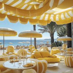 an outdoor seating area with yellow and white striped umbrellas over the tables on the beach