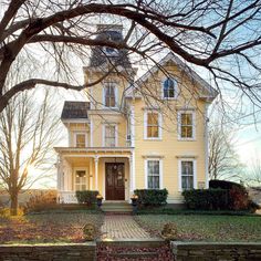 a large yellow house sitting next to a leaf covered tree in front of a fence