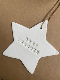 a white ceramic star ornament with the words best teacher on it hanging from a string