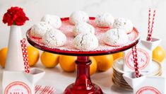 a red plate topped with snowball cookies on top of a table next to oranges