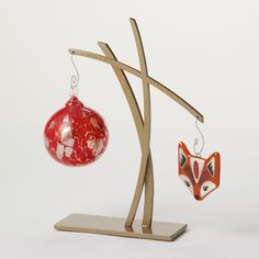 two ornaments are hanging from a wooden stand on a white surface, one has a red ornament and the other is a fox