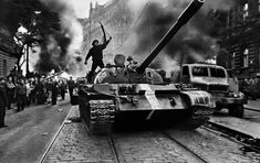 a man standing on top of a tank in the middle of a street surrounded by people