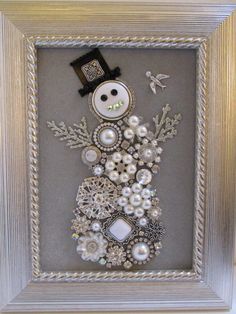 a snowman made out of buttons and other items in a silver frame on the wall