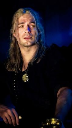 a man with long hair wearing a black shirt and holding a gold ring in his hand