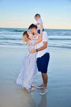 a man and woman holding a baby on the beach