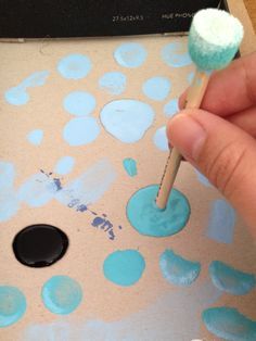 a person is holding a pencil and painting on a piece of cardboard with blue dots