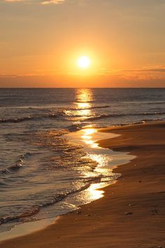 the sun is setting over the water at the beach with waves coming in to shore