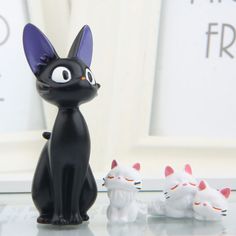 a black cat figurine sitting next to four white kittens on a table