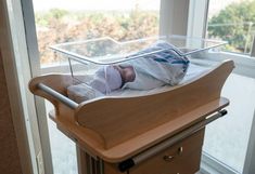 a baby laying in a crib next to a window with an open glass pane