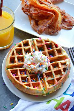 a waffle with whipped cream and sprinkles sits on a plate next to a glass of orange juice