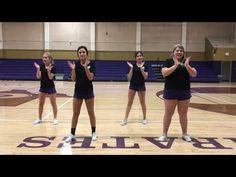 four girls in black shirts and blue shorts on a basketball court with their hands up