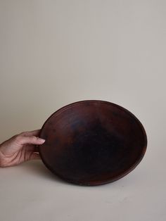 a person holding a wooden bowl in front of a white wall with a hand on it