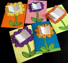 four different colored cards with flowers cut out of them on a black surface, one has a hole in the middle