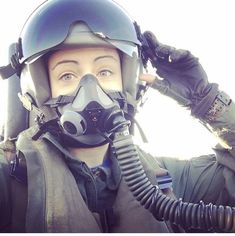 a woman wearing a gas mask and holding her hand up to her face with the air force pilot's helmet on