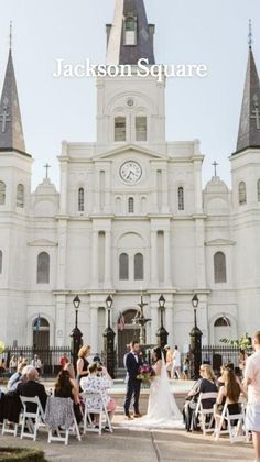 a wedding ceremony in front of a large white building with steeples on it's sides