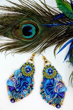 a pair of peacock feathers with blue and green beaded earrings on top of it