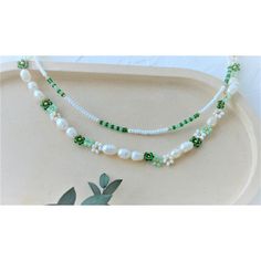 three strands of white pearls and green glass beads on a platter with leaves in the background